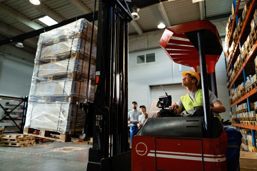 operador-de-montacargas-cargando-carga-mientras-trabaja-en-un-almacen-sus-colegas-estan-en-el-fondo
